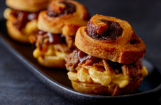 Three cinnamon roll sandwiches filled with pulled pork and mac & cheese on a black platter.